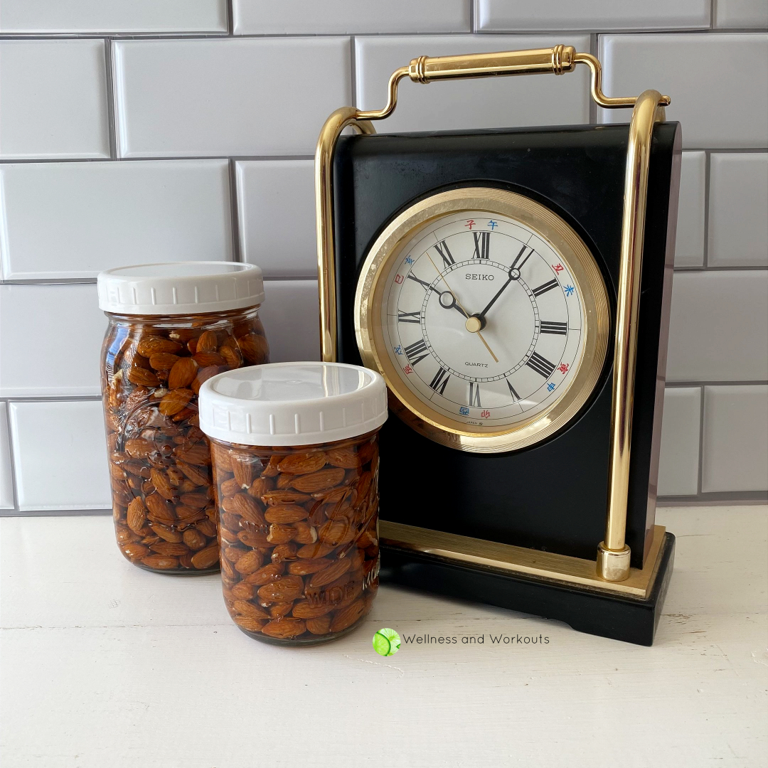 Two jars full of organic raw almonds and filtered water sit near a clock.